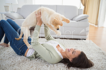 Woman lifting puppy while lying on rug