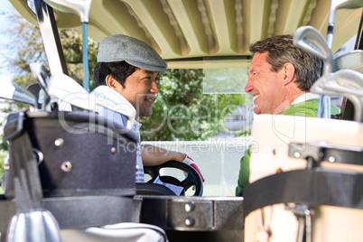 Golfing friends driving in their golf buggy smiling to each othe