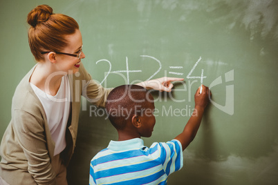 Teacher assisting boy to write on blackboard in classroom