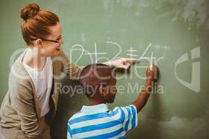 Teacher assisting boy to write on blackboard in classroom