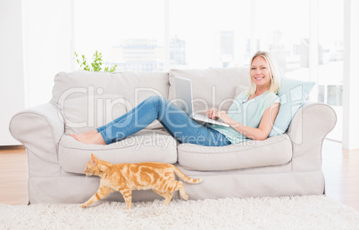 Woman using laptop on sofa while cat passing by