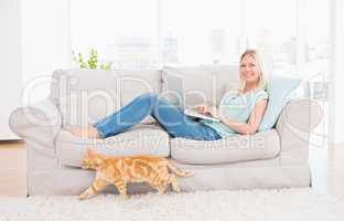 Woman using laptop on sofa while cat passing by
