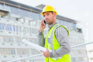 Architect with blueprints using mobile phone against building