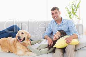 Happy couple with dog relaxing on sofa