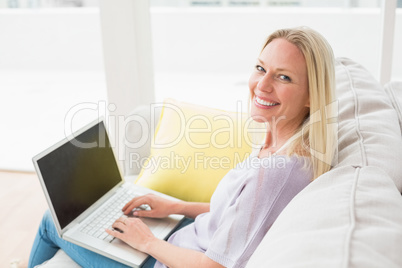 Smiling woman on sofa using laptop in living room