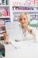 Smiling pharmacist thinking and reading prescription