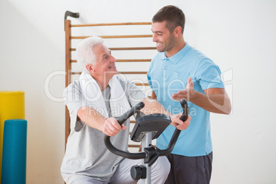 Senior man doing exercise bike with his trainer