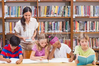 Pretty teacher helping pupils in library