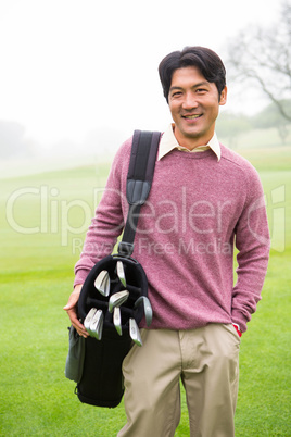 Golfer standing holding his golf bag smiling at camera