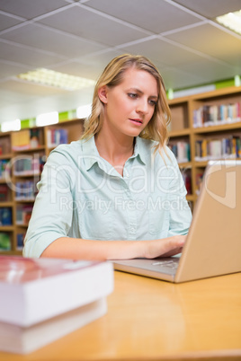Pretty student studying in the library with laptop