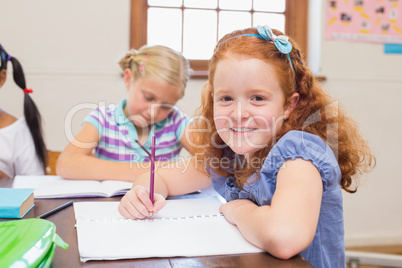 Cute pupils writing at desk in classroom