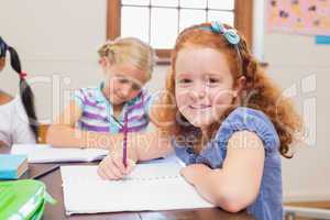 Cute pupils writing at desk in classroom