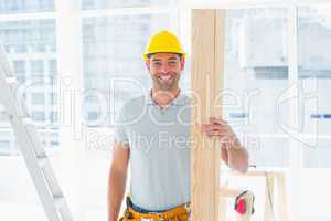Smiling male carpenter holding plank in building