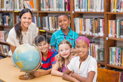 Cute pupils and teacher looking at globe in library