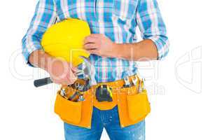 Manual worker wearing tool belt while holding hammer and helmet