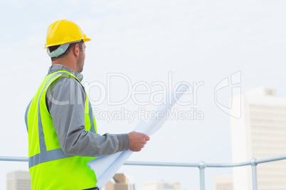 Architect in protective workwear holding blueprints outdoors