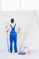 Handyman with paint roller examining wall at home