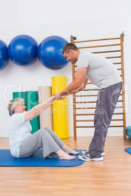 Trainer working with senior woman on exercise mat