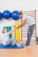 Trainer working with senior woman on exercise mat