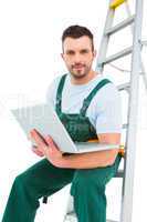 Carpenter sitting on ladder using laptop