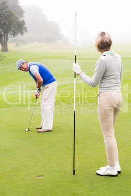 Lady golfer holding flag for partner putting ball