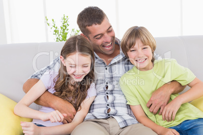 Father tickling children while sitting on sofa