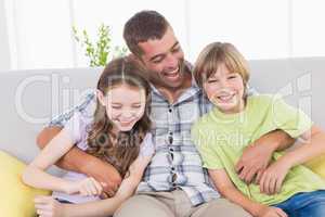 Father tickling children while sitting on sofa