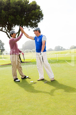 Golfing friends high fiving on the hole