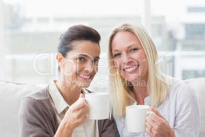 Smiling female friends having coffee in living room