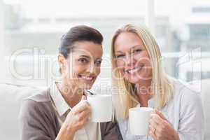 Smiling female friends having coffee in living room