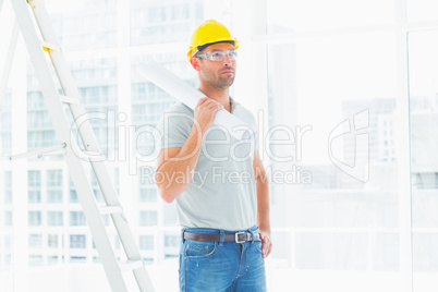 Handyman holding rolled up blueprint in bright office