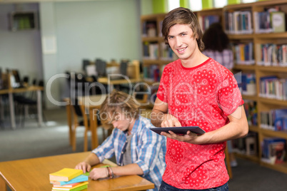 Male college student using digital tablet in library