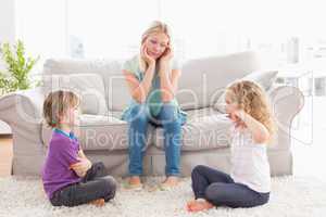 Upset mother looking at children fighting on rug
