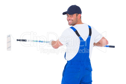 Handyman in overalls using paint roller on white background