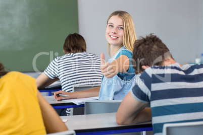 Beautiful female student gesturing thumbs up in class