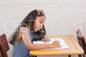 Cute pupils writing at desk in classroom