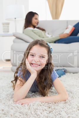 Happy girl lying on rug while mother relaxing at home