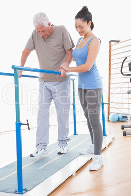 Senior man walking with parallel bars and coach help