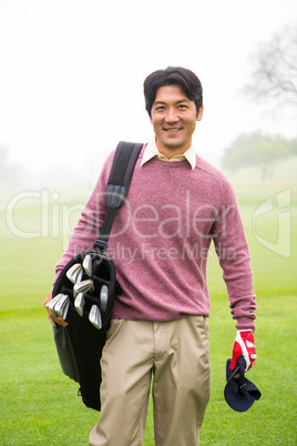 Golfer standing holding his golf bag smiling at camera