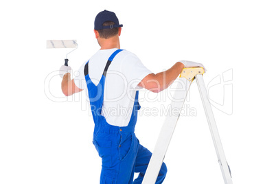 Handyman climbing ladder while using paint roller