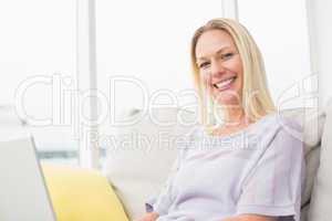 Smiling woman with laptop sitting on sofa