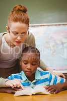 Teacher assisting little boy with homework in classroom
