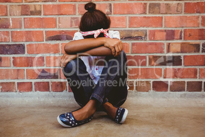 Tensed girl sitting against brick wall in school corridor