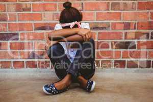 Tensed girl sitting against brick wall in school corridor