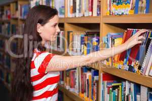 Pretty student taking book from shelf in library