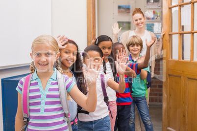 Cute pupils waving at camera in classroom