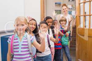 Cute pupils waving at camera in classroom