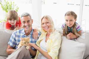 Happy family sitting with cat on sofa at home
