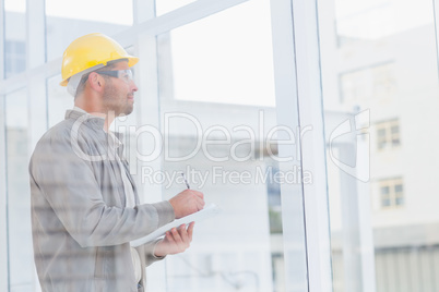 Architect writing on clipboard while looking through office wind