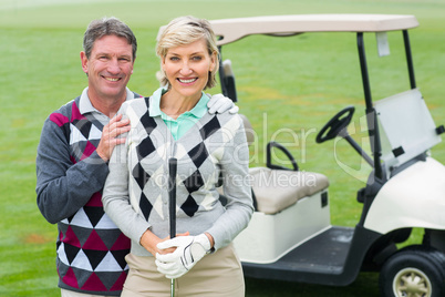 Happy golfing couple with golf buggy behind